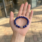 Macro shot of the lapis lazuli cross bracelet resting flat inside an open palm upward showing fine jewelry details.