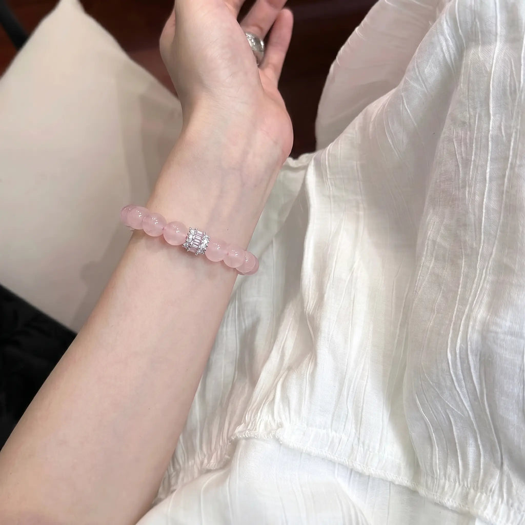 Close-up shot of the madagascar rose quartz beaded bracelet adorned on an open palm upward wrist extension over white pleated fabric.