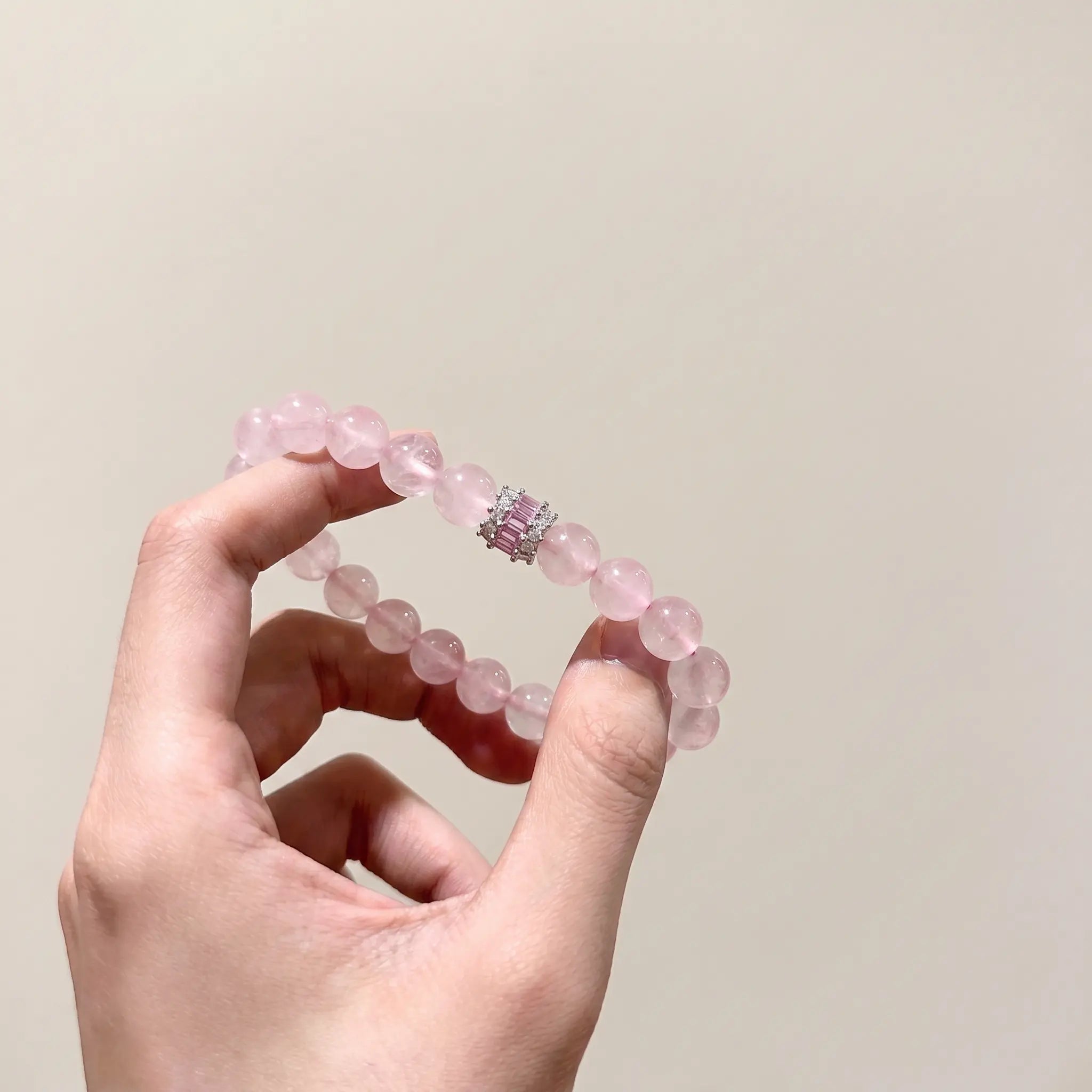 Detailed macro shot of the Madagascar rose quartz bracelet held in a single hand to showcase translucent pink beads.