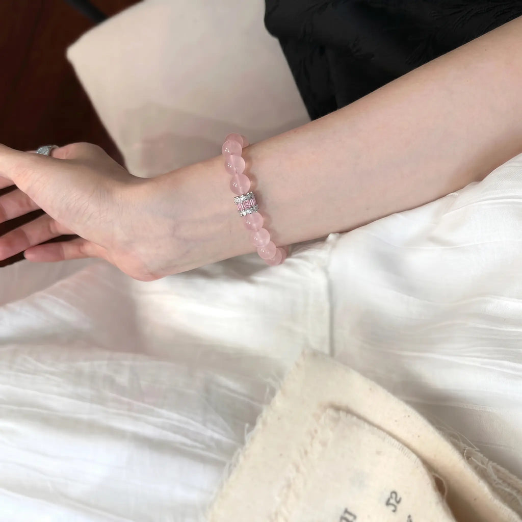 Close-up shot of the madagascar rose quartz beaded bracelet adorned on a left wrist extended diagonally over elegant white pleated fabric.