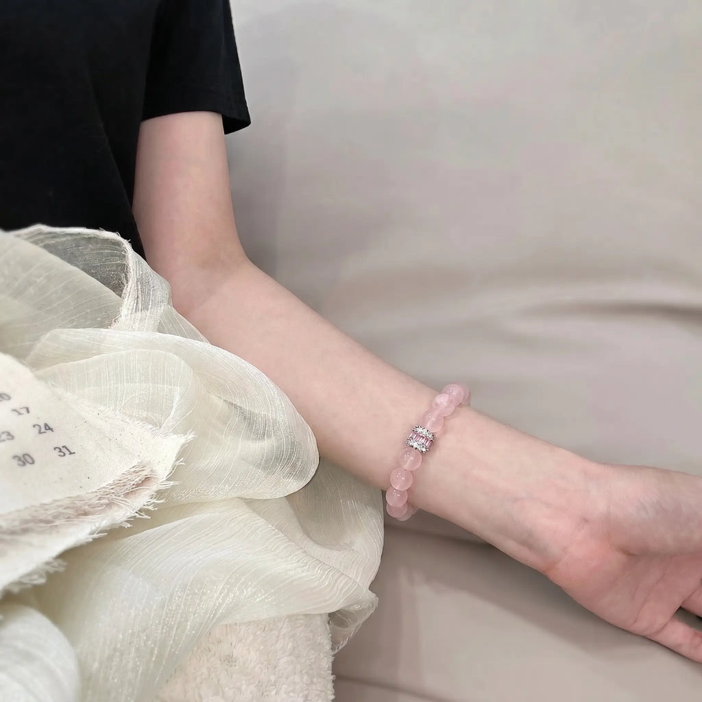 Close-up shot of the Madagascar rose quartz bracelet adorned on a left arm extended diagonally beside elegant white textured fabric.
