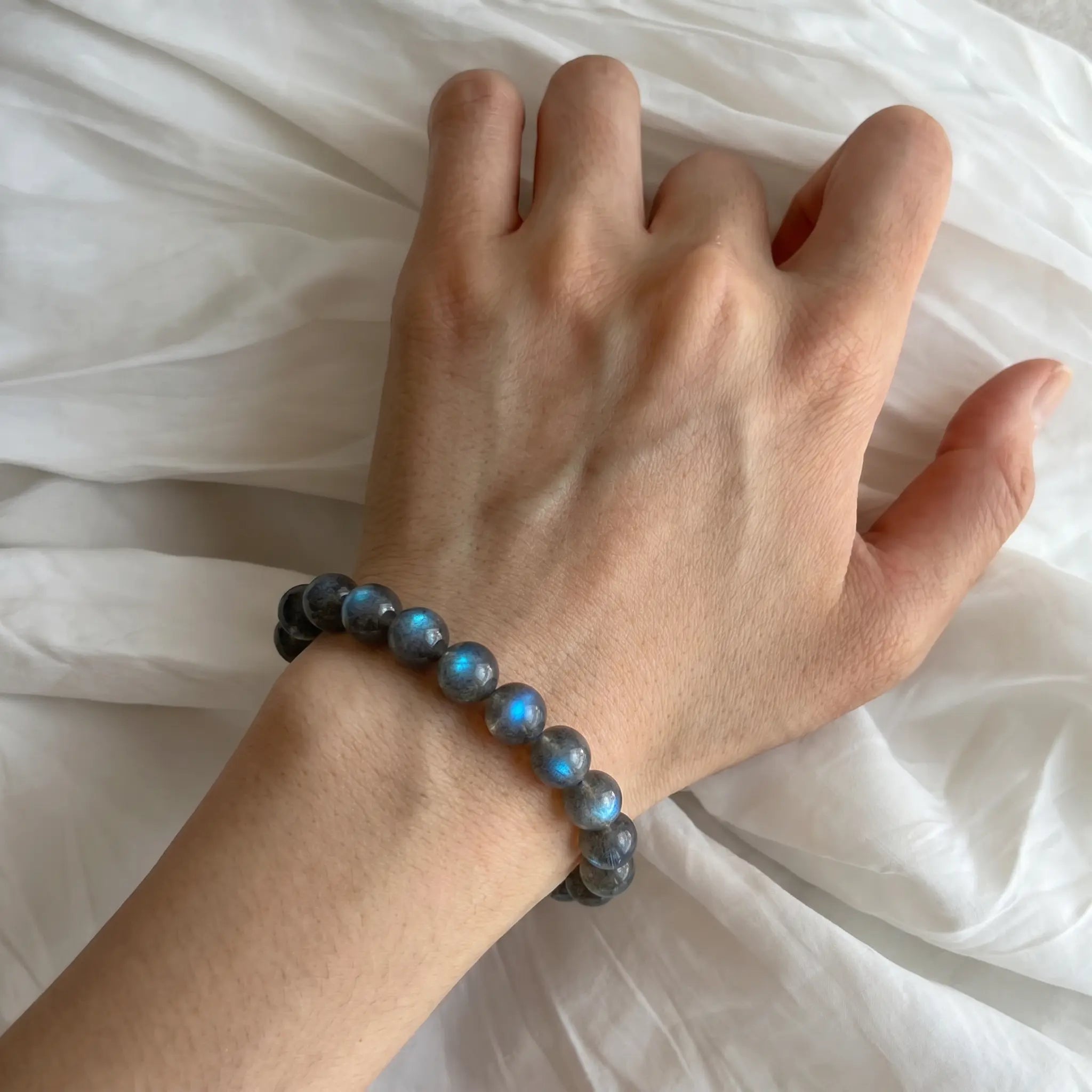 Close-up shot of a female wrist wearing the Mystic Moonstone Bracelet resting gracefully over elegant white wrinkled fabric.