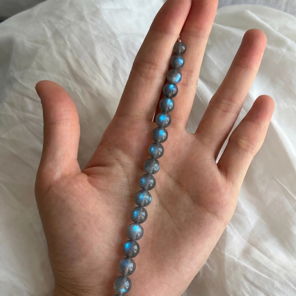 Detailed shot of an unstrung line of Mystic Moonstone Bracelet beads resting flat inside an open palm upward.