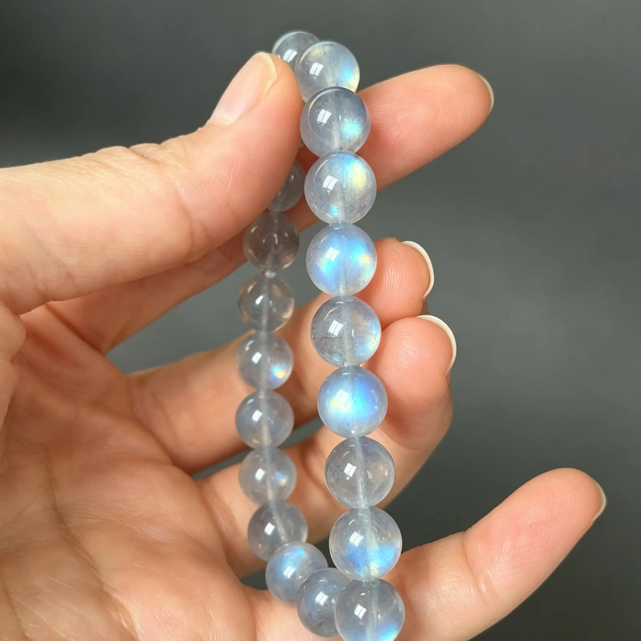 Close-up shot of a hand holding a natural moonstone labradorite beaded bracelet with strong blue flashes.