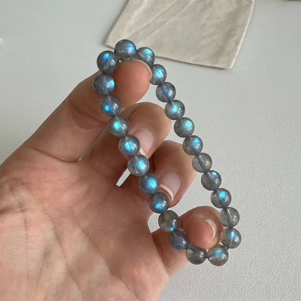 Close-up shot of fingers holding a genuine Mystic Moonstone Bracelet showing electric blue flash luminosity.