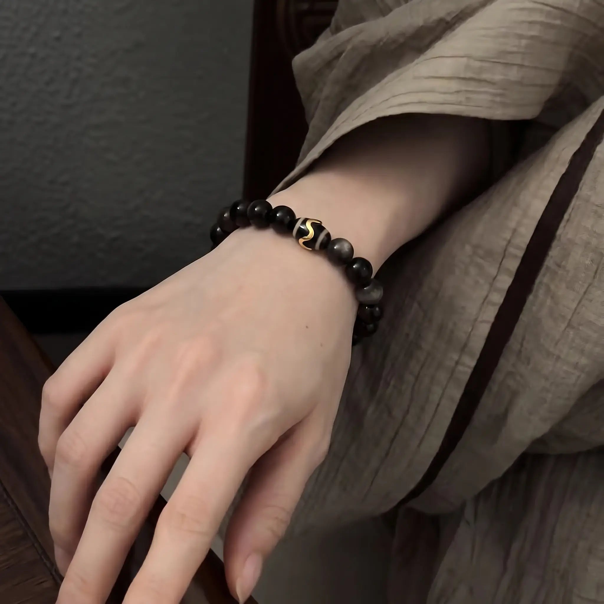 Enlarged diagonal shot from upper-right to lower-left showcasing a black crystal protection bracelet on a woman hand.