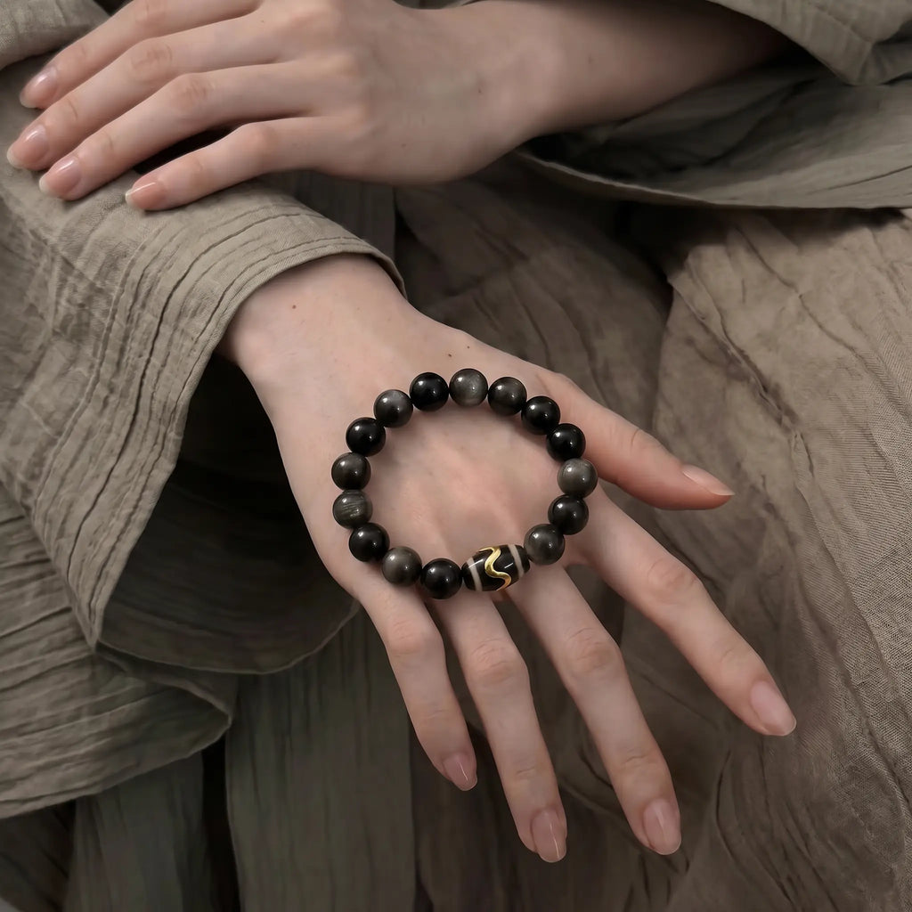 Macro shot of the black obsidian bracelet resting flat over the smooth knuckles and back of a female hand.