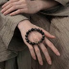 Macro shot of the black obsidian bracelet resting flat over the smooth knuckles and back of a female hand.