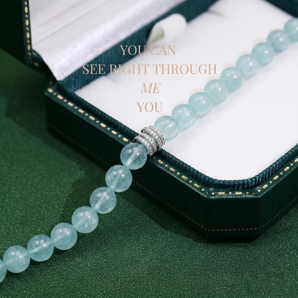 An unstrung straight line layout of natural aquamarine gemstone beads placed horizontally over a clean desk.