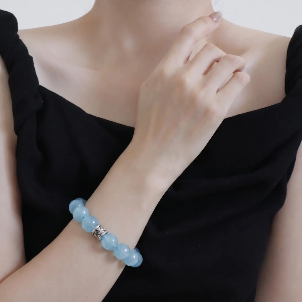 Close-up shot of overlapping arms gracefully displaying the ocean’s grace aquamarine bracelet against a black off-the-shoulder top.