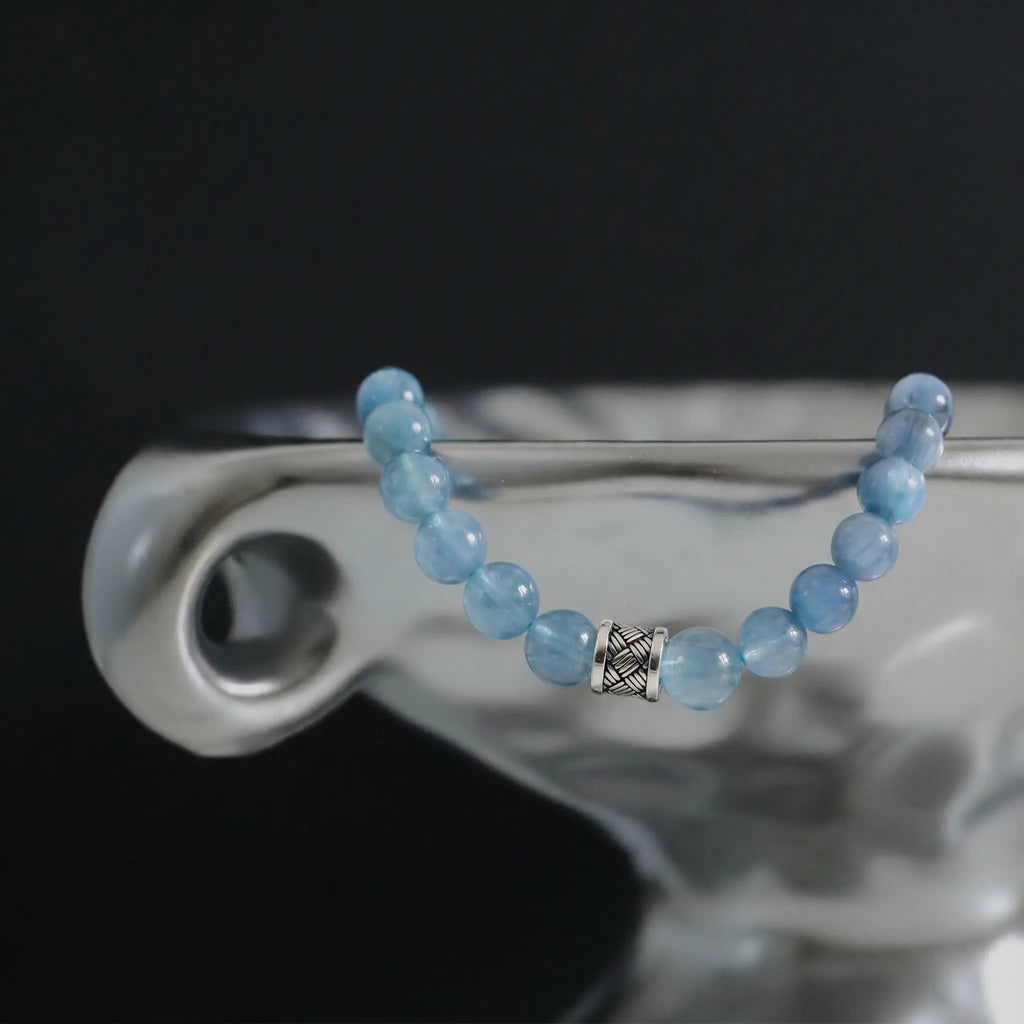 The ocean s grace aquamarine bracelet displayed elegantly draped over a vintage shiny silver enameled metal dish edge.