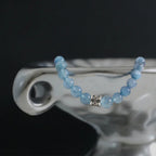 The ocean s grace aquamarine bracelet displayed elegantly draped over a vintage shiny silver enameled metal dish edge.