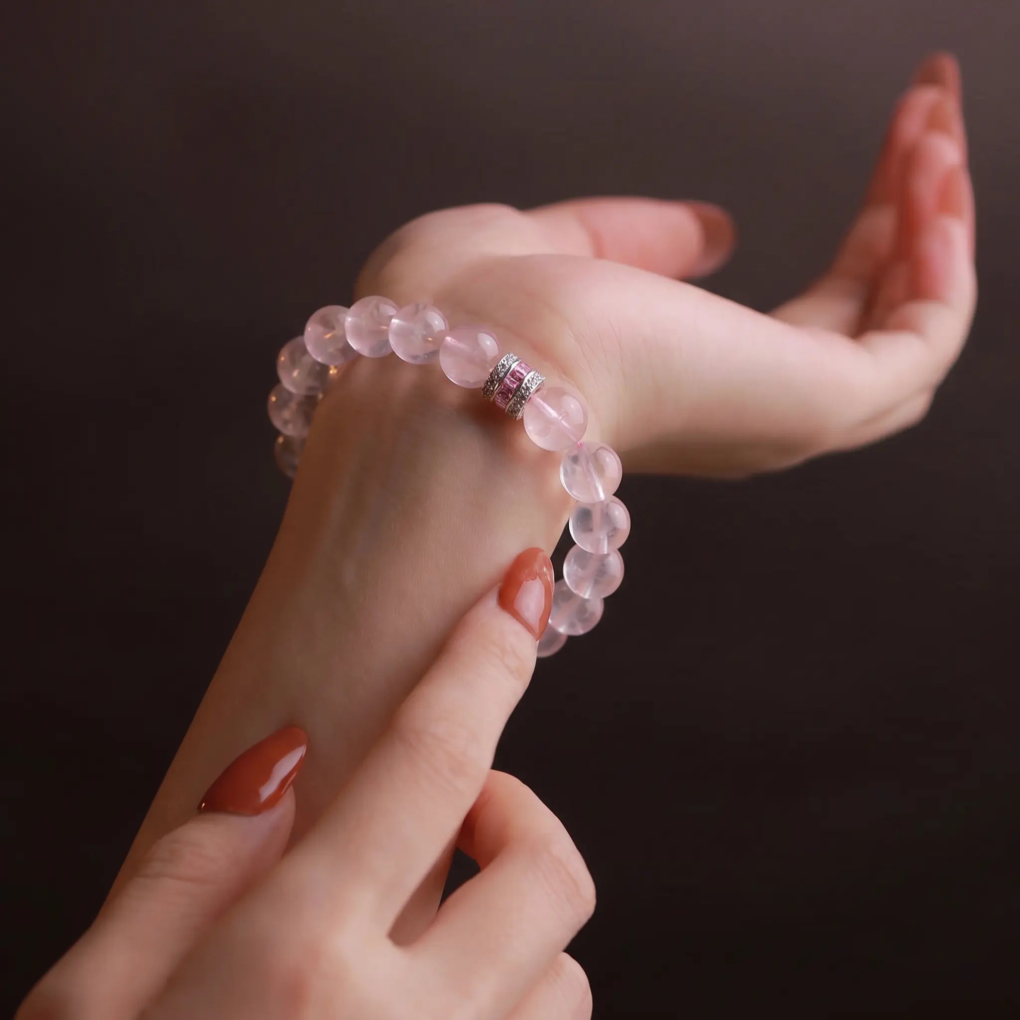 Front close-up view of a woman wrist wearing the Pure Heat rose quartz bracelet with her right fingers gently touching the beads.