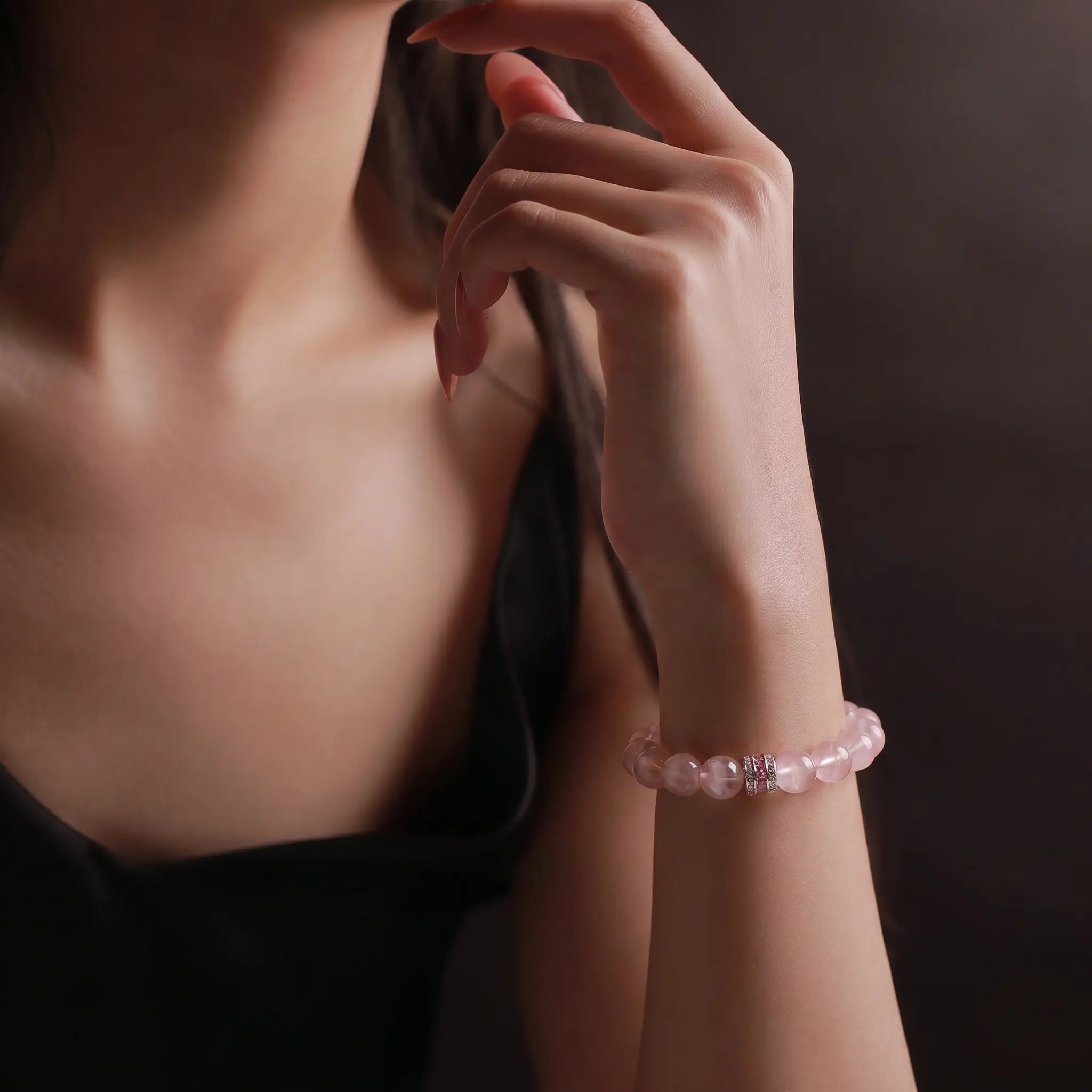 Front portrait view up to the chin showing an elegant lady wearing the Pure Heat rose quartz bracelet styled with a black camisole top.