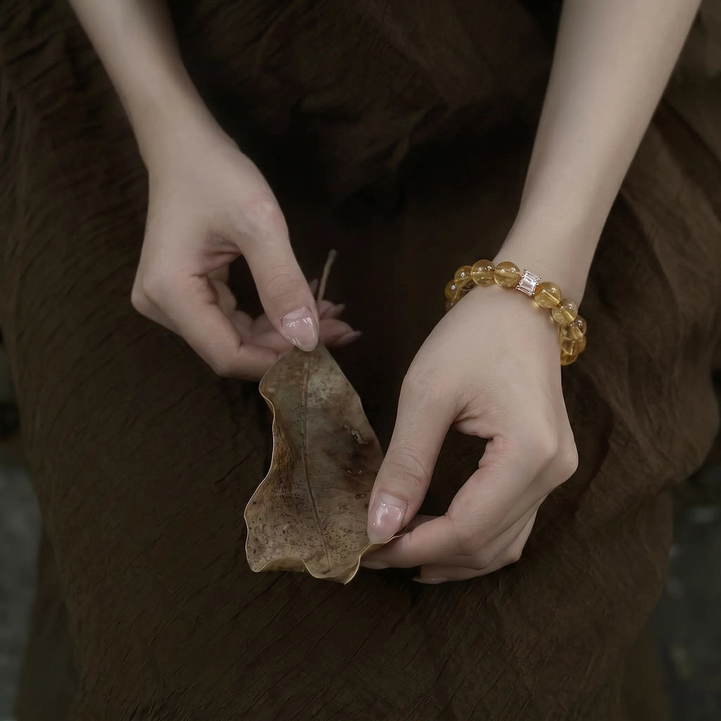 Top-down high angle close-up of a woman cupping an organic green leaf with her hands showing a citrine gemstone bracelet.