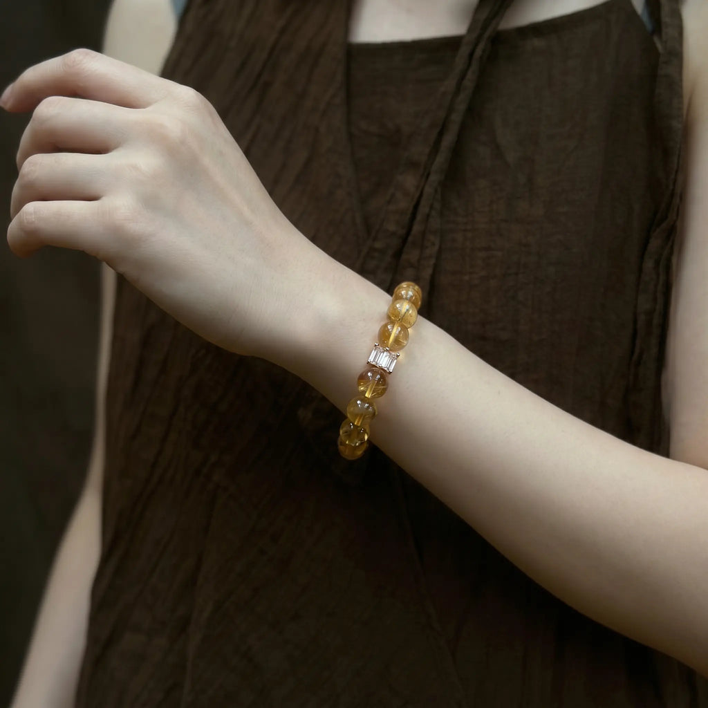 Side profile shot from upper body to shoulder showing a lady raising her left hand to display a yellow crystal bracelet.
