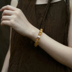 Side profile shot from upper body to shoulder showing a lady raising her left hand to display a yellow crystal bracelet.