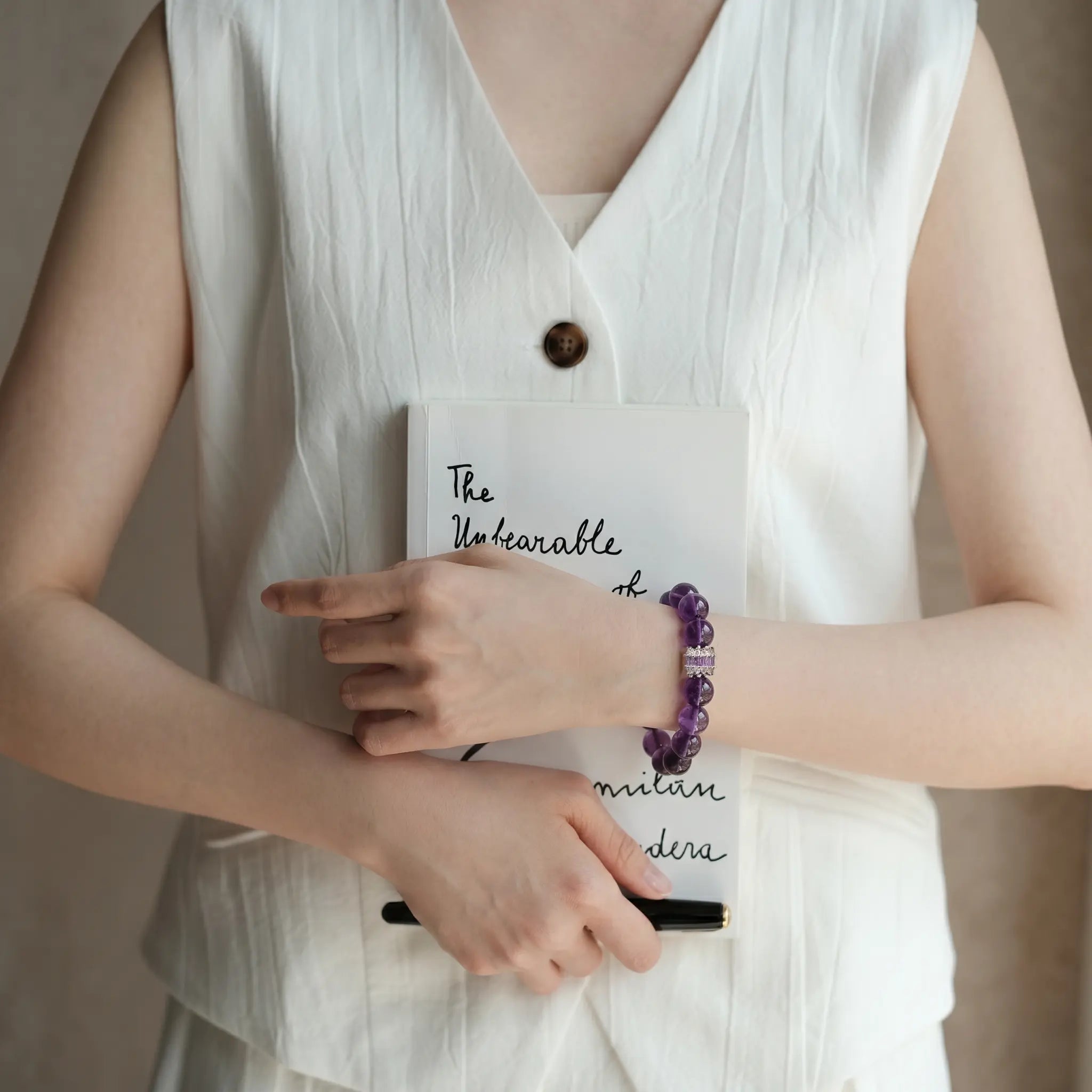 Front portrait shot to the shoulders of a lady clutching a book to her chest revealing her purple quartz bracelet.