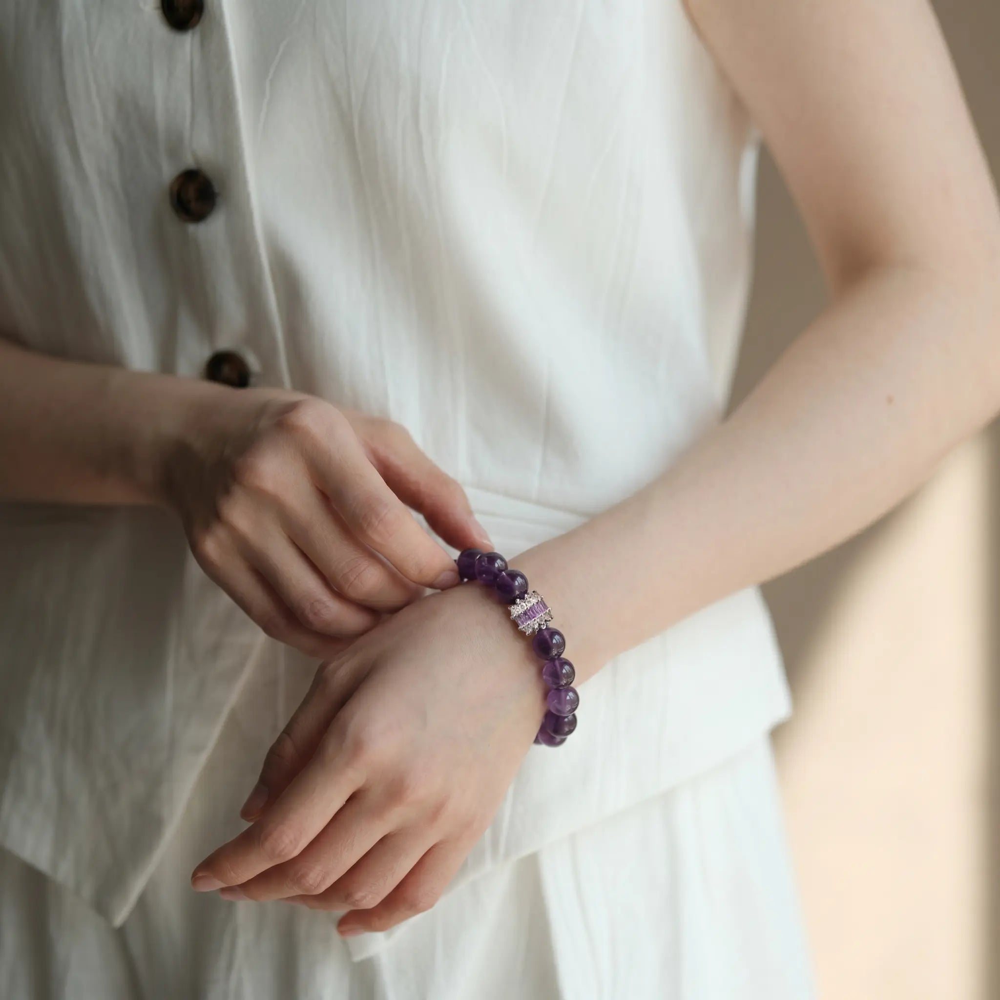 Front crop to the chest showing a bent left arm across the abdomen while the right hand touches the amethyst wrist bracelet.