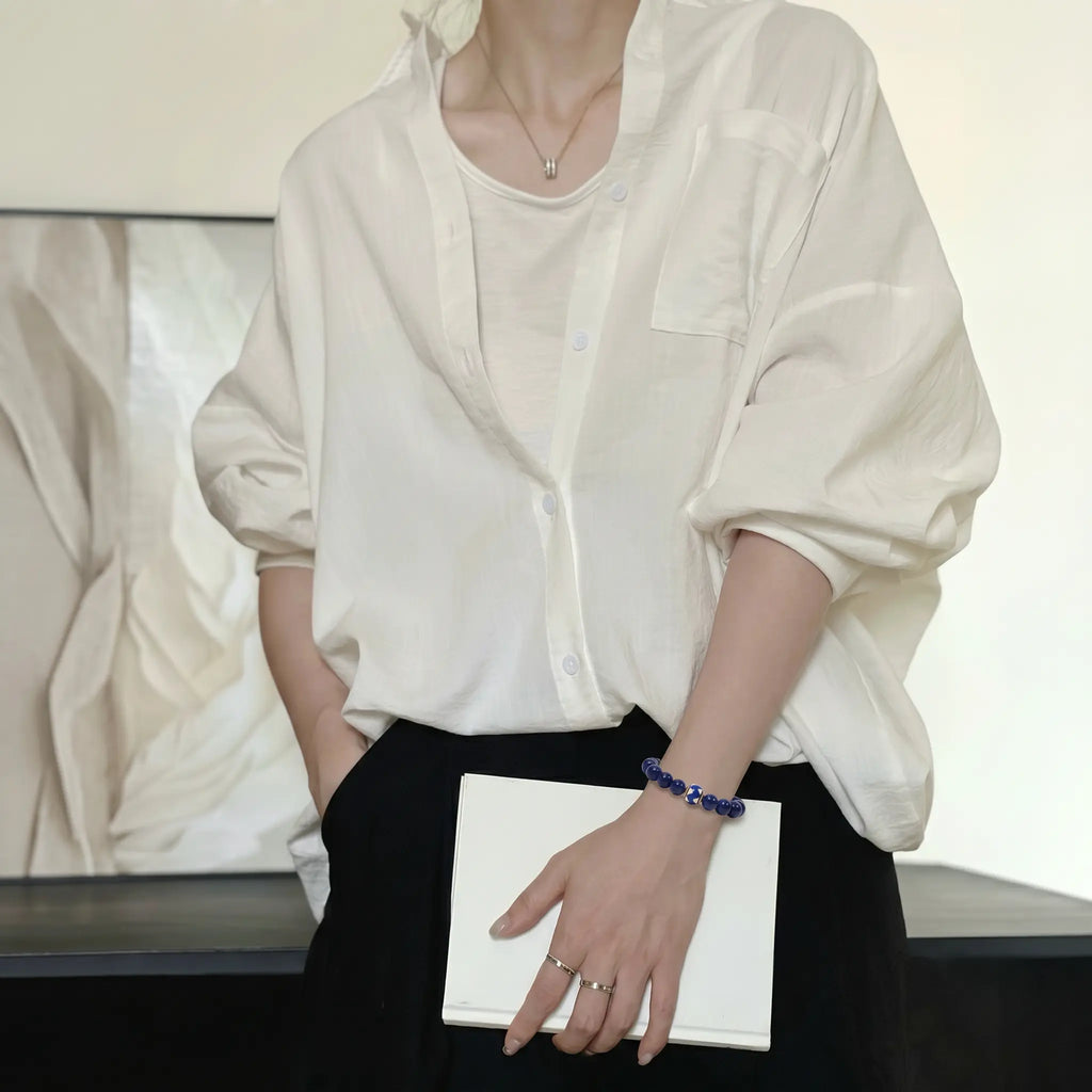 Mid-shot portrait of a woman holding a book over her dress while her right hand is tucked into a pants pocket.