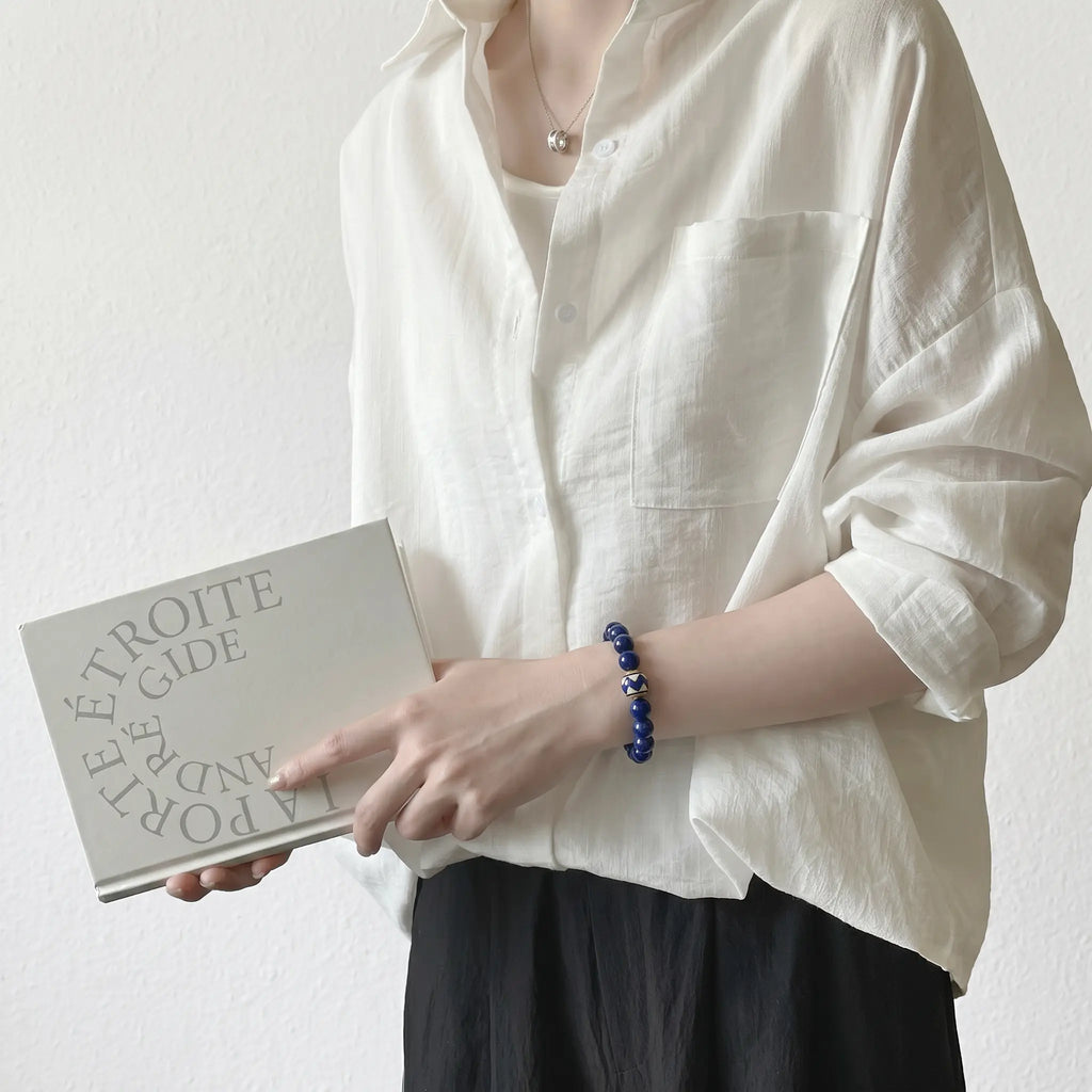 Three-quarter upper body shot of a elegant lady holding a hardcover book showcasing her blue mineral gemstone bracelet.
