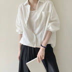 Mid-shot portrait of a lady in a dress holding a book in front of her skirt with her right arm relaxed beside her leg.