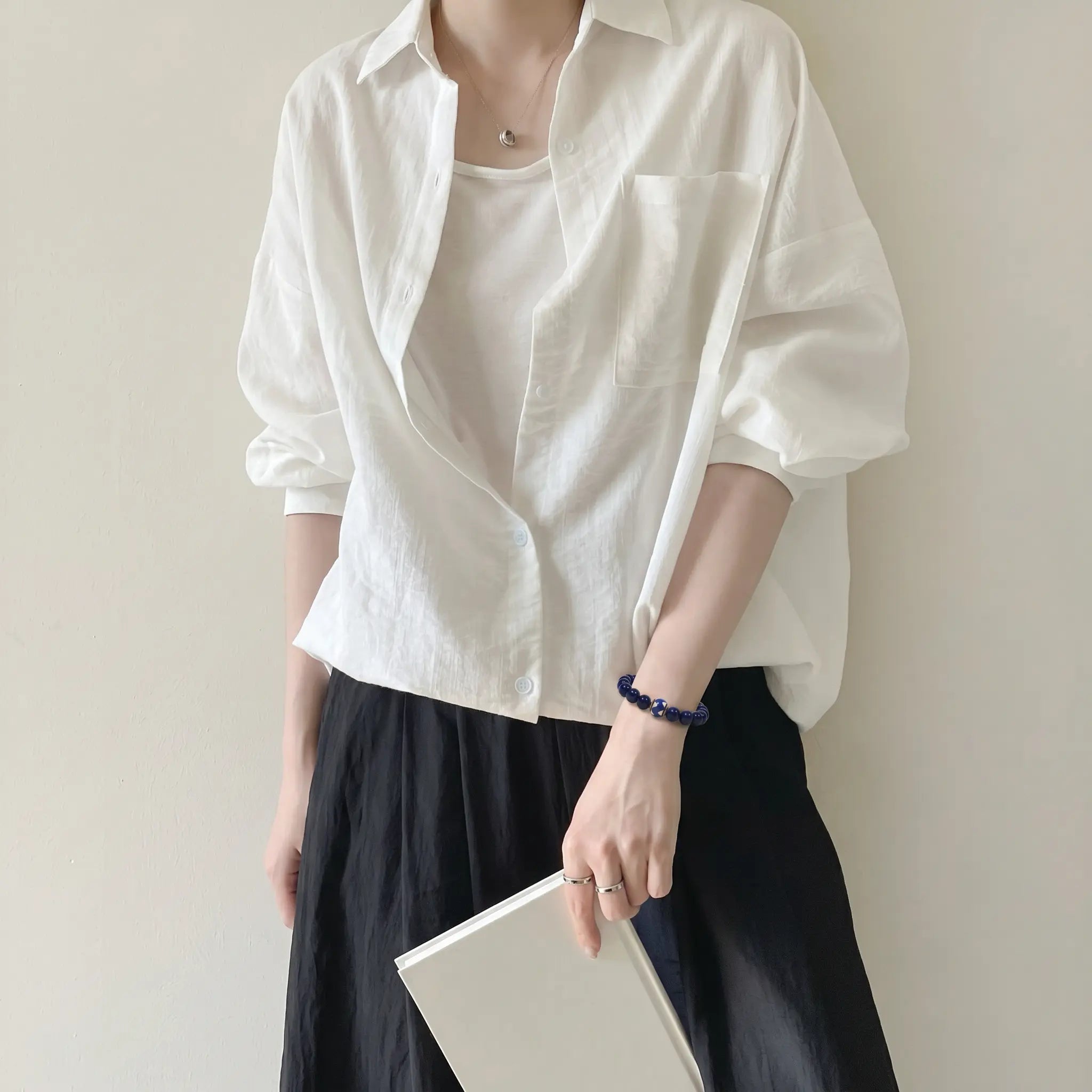 Mid-shot portrait of a lady in a dress holding a book in front of her skirt with her right arm relaxed beside her leg.