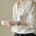 Cropped upper body view of a woman holding a porcelain coffee cup with a book tucked under her arm showing the crystal bracelet.