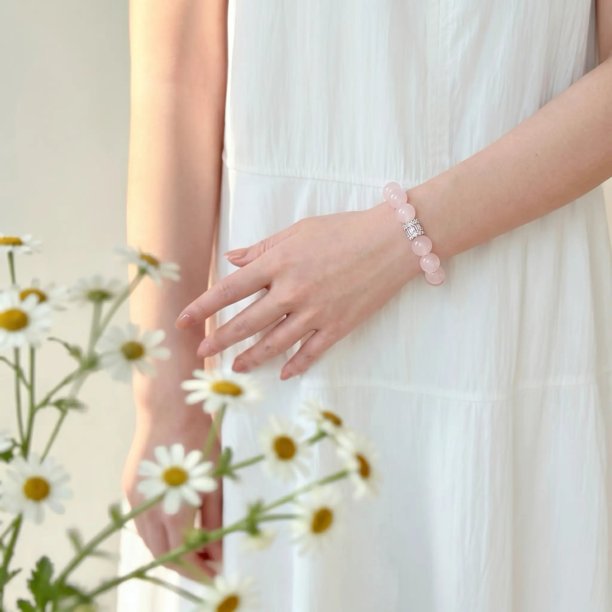 Front view cropped from hips to elbows showing overlapping hands with the left hand touching a relaxed right wrist wearing a crystal bracelet.