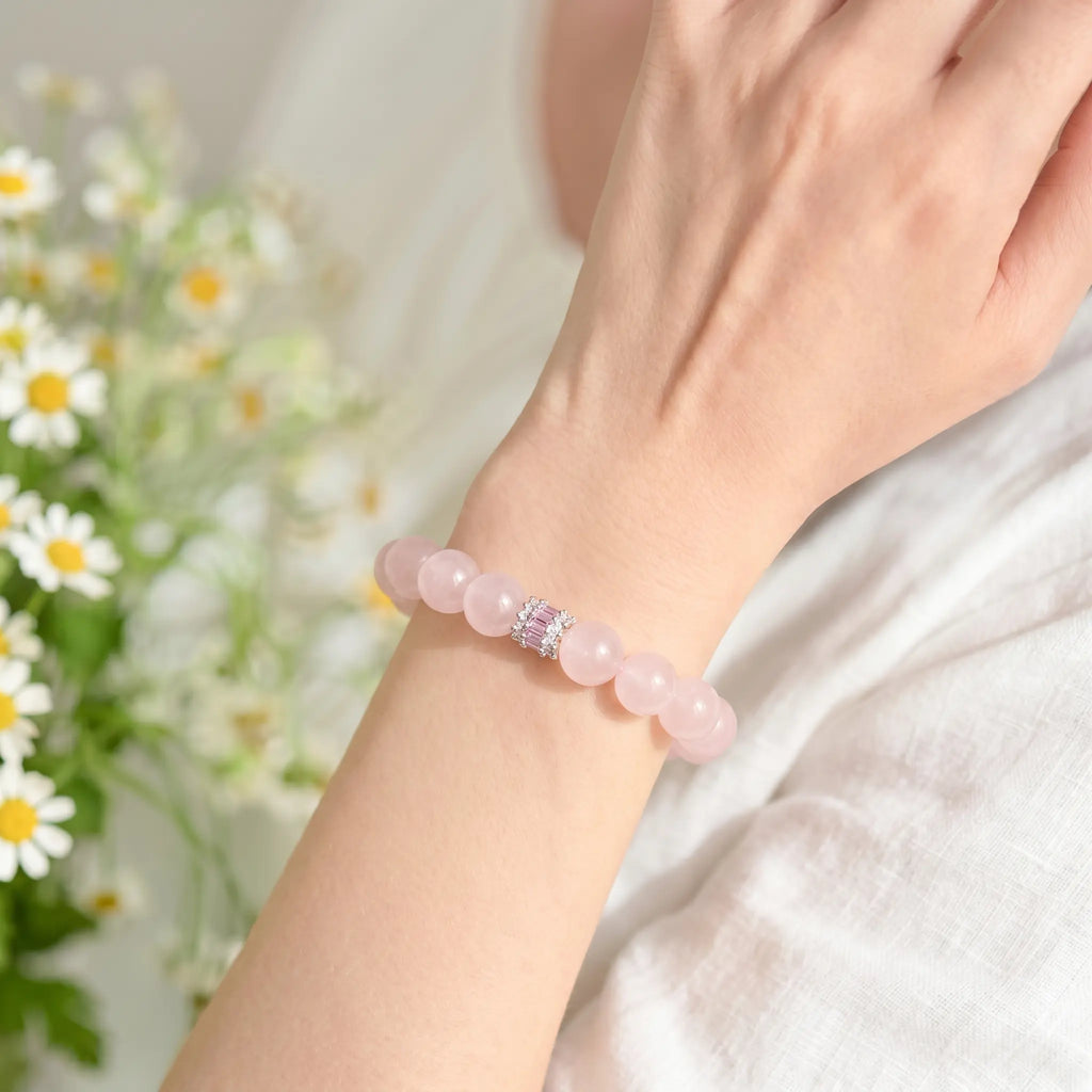 Left-side close-up view of an elegant woman raising her left wrist to showcase a pink crystal quartz bracelet.
