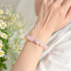 Left-side close-up view of an elegant woman raising her left wrist to showcase a pink crystal quartz bracelet.
