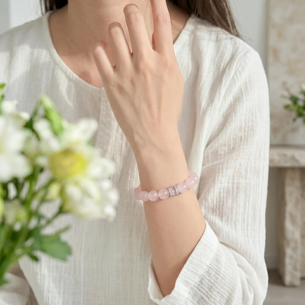 Front portrait shot to the shoulders showing a woman with her elbow on a desk and raised forearm displaying a pink gemstone bracelet.