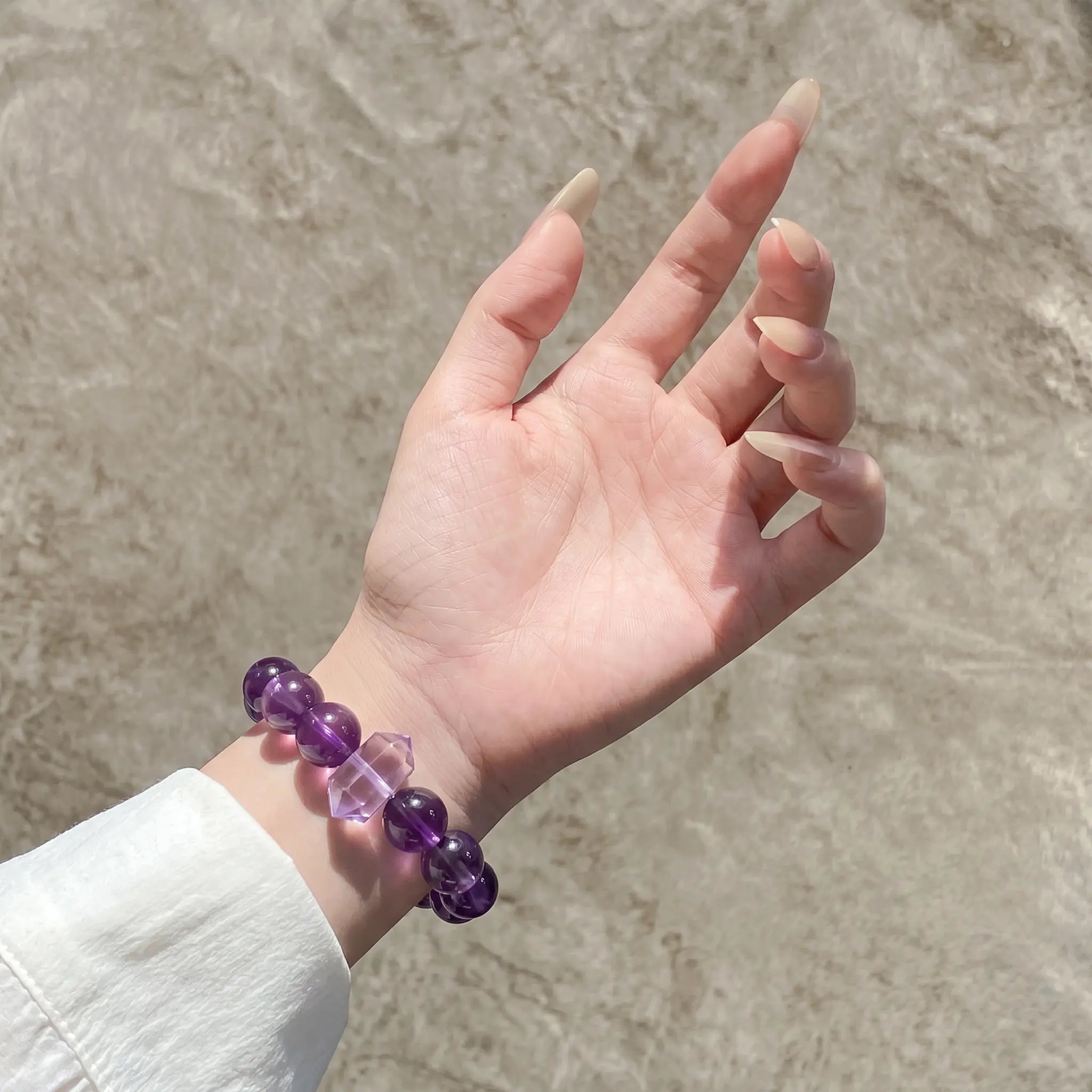 Detailed shot extending from lower-left to center focusing on an open palm upward revealing a purple quartz bracelet on the wrist.