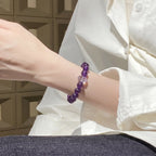 Left-side perspective of a woman with her left elbow resting on a desk and raised forearm showing an amethyst gemstone bracelet.