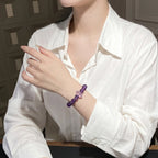 Left-side profile view of overlapping hands with a raised left forearm displaying a purple crystal bracelet.