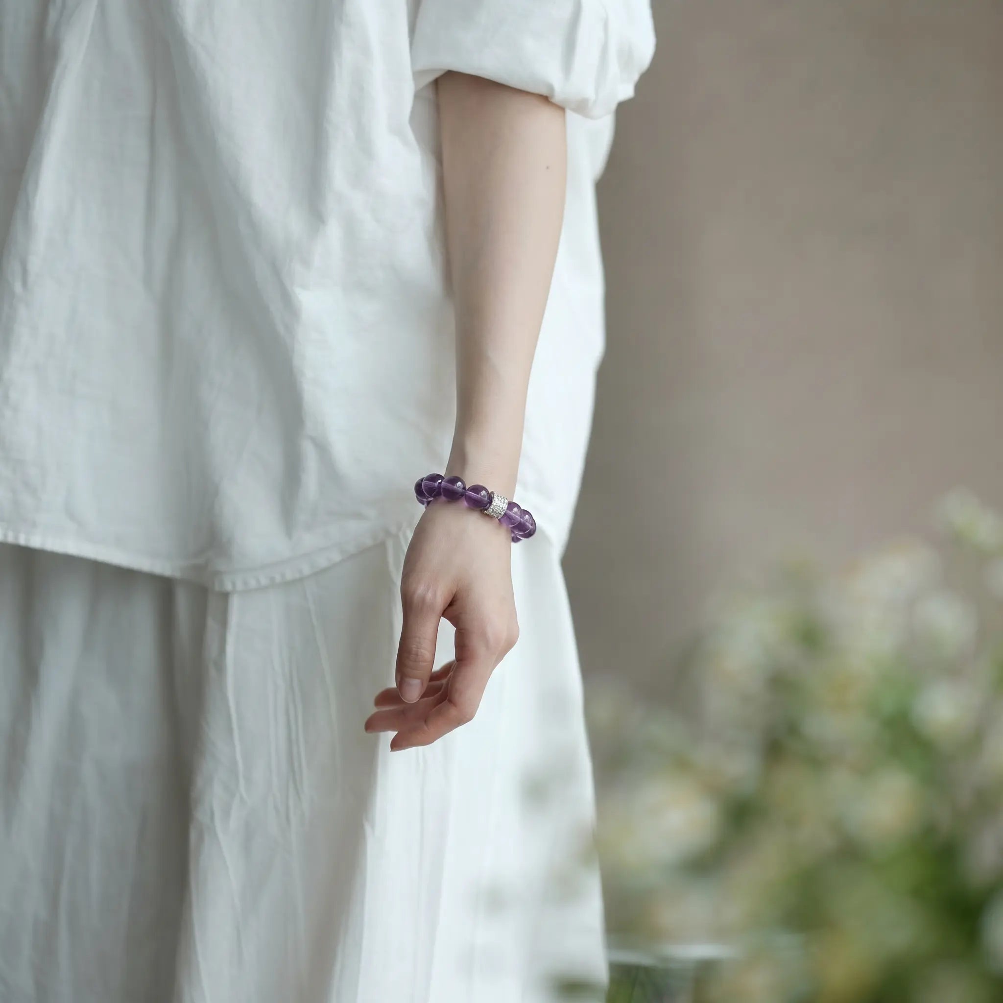 Detailed close-up shot of a female left hand resting naturally downward showcasing a premium purple gemstone crystal bracelet.