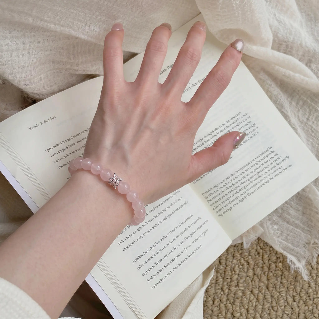 Macro texture view of Serenity Heart pink quartz bracelet on a resting hand pressing down on book sheets.