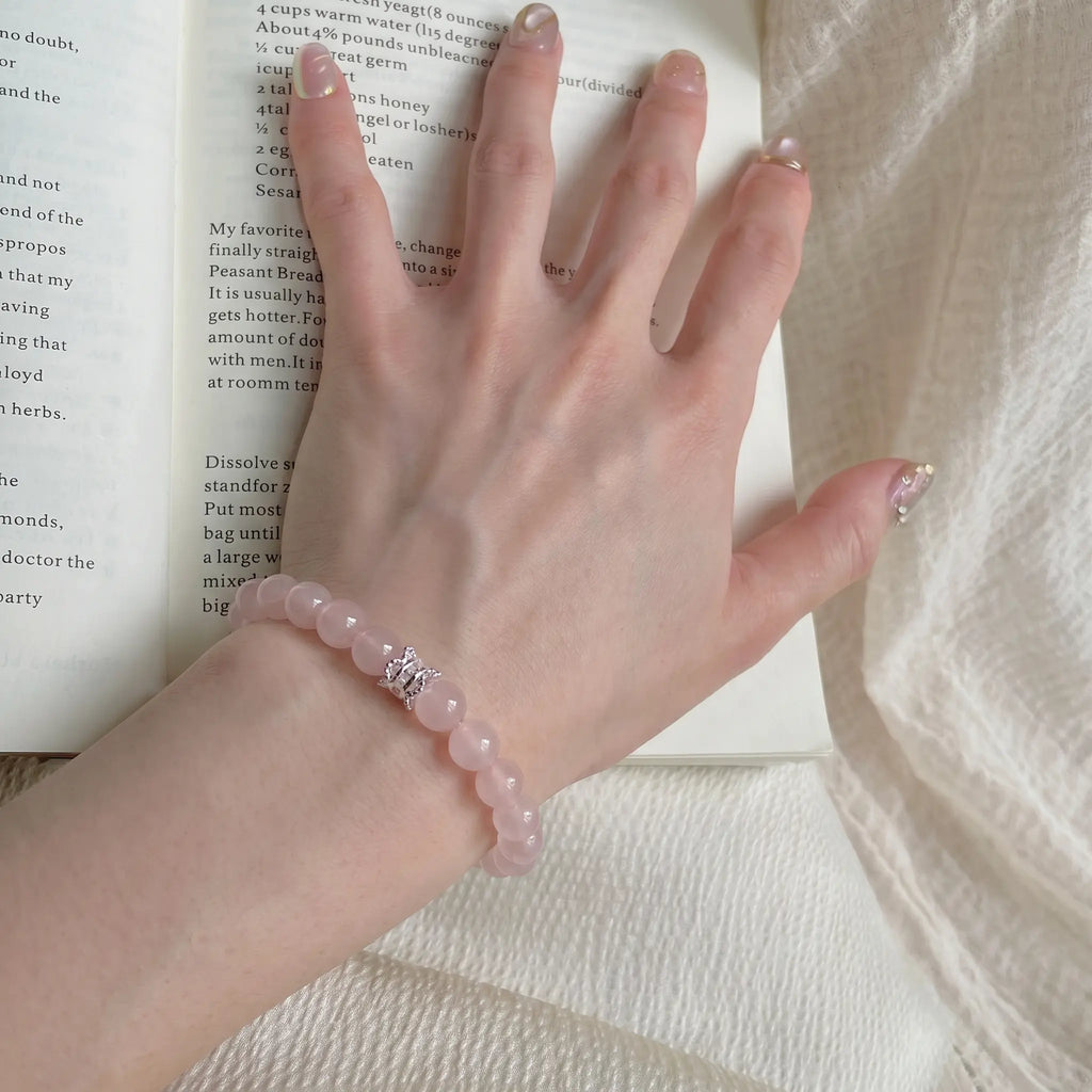 Extreme close-up from the lower-left angle focusing on pink quartz beads with a book beneath the hand palm.
