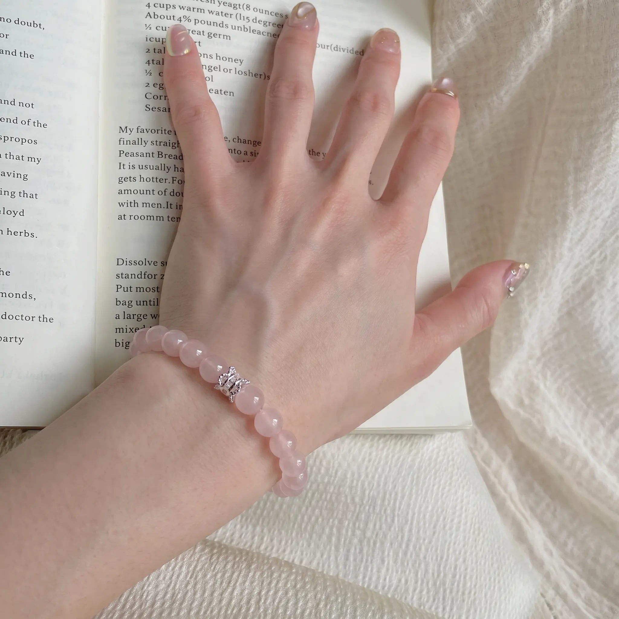 Extreme close-up from the lower-left angle focusing on pink quartz beads with a book beneath the hand palm.