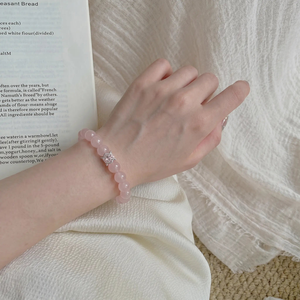 Lower-left diagonal perspective close-up showing the detail of a smooth pink gemstone bracelet on a woman wrist.