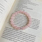 Top-down detail shot showcasing a natural pink gemstone crystal bracelet resting flat on text-covered book paper.