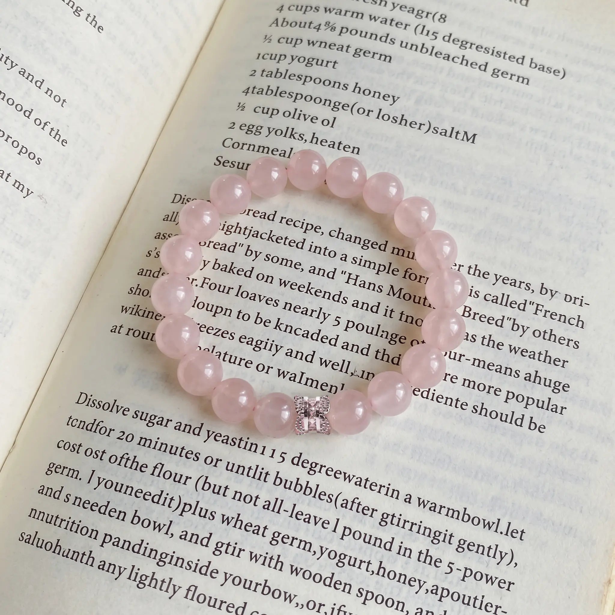 Top-down detail shot showcasing a natural pink gemstone crystal bracelet resting flat on text-covered book paper.