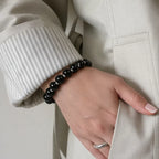 Close-up of a woman hand tucked in a pants pocket revealing a black obsidian beaded bracelet on her wrist.