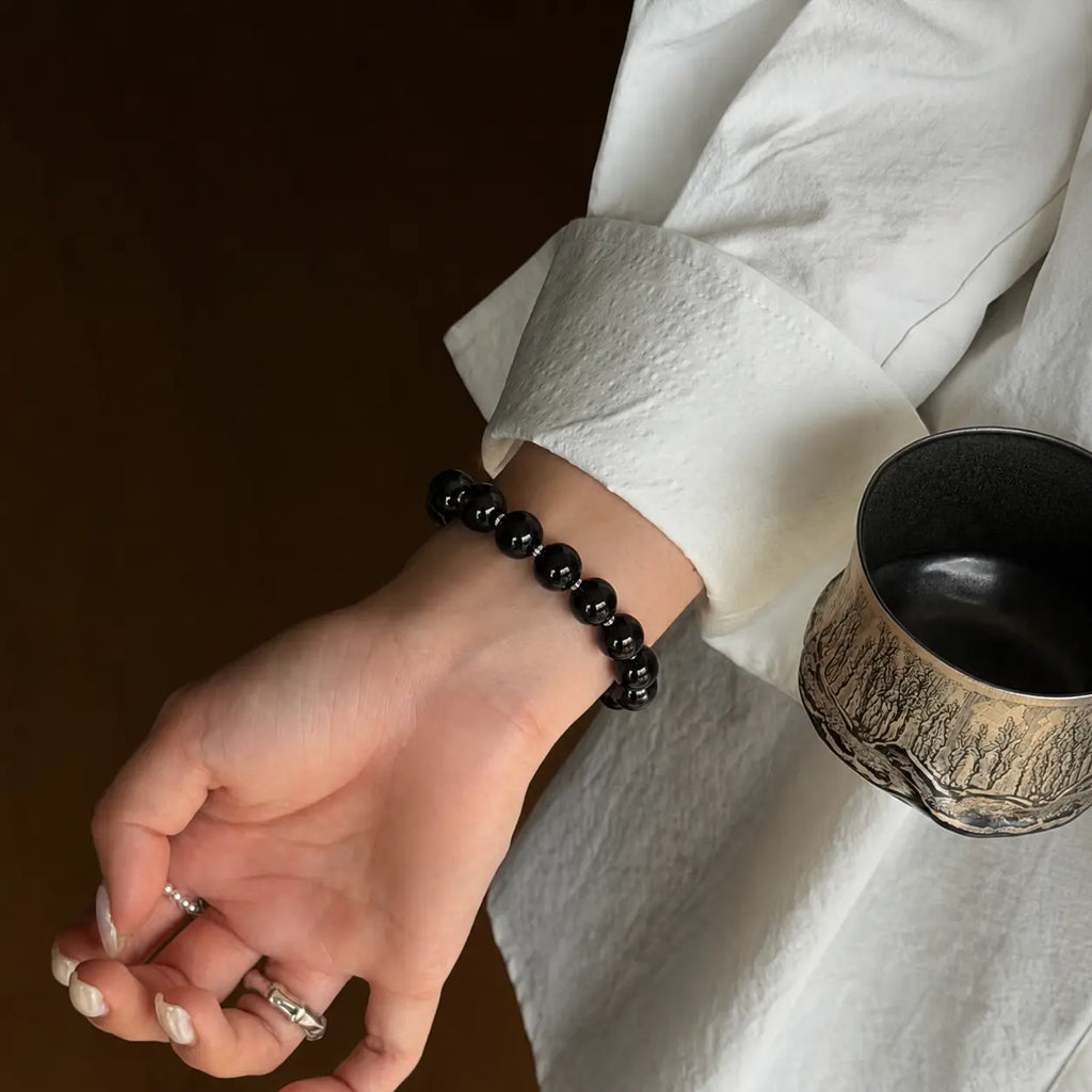 Upper-right diagonal close-up shot focusing on a woman wrist with a black protective crystal bracelet and open palm.