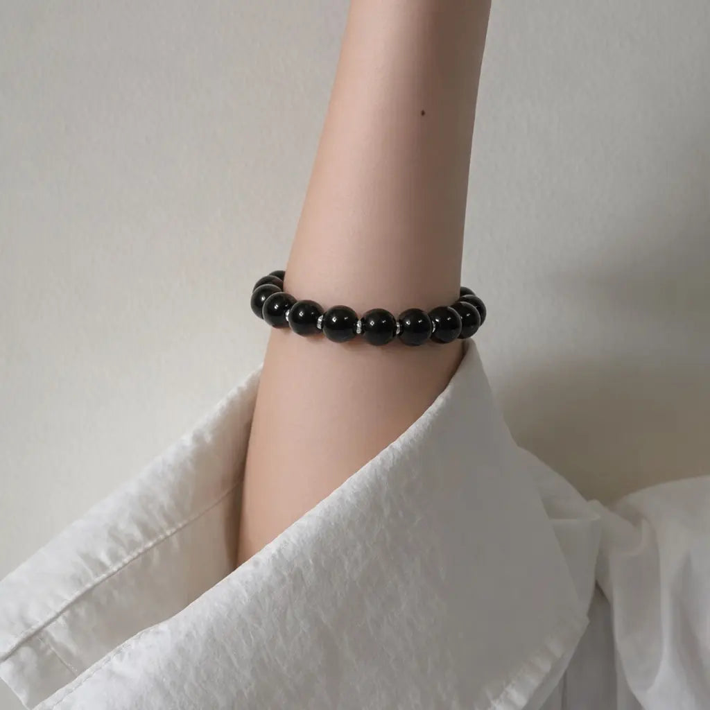 A raised elbow perspective showcasing the minimalist black obsidian gemstone bracelet on a vertical arm.
