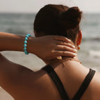 Rear perspective crop from shoulders to head showing a lady touching the nape of her neck revealing a crystal bracelet.