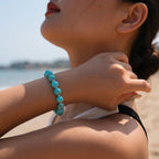 Low-angle profile view of a lady tilting her head back while a raised hand touches her throat showing a gemstone bracelet.