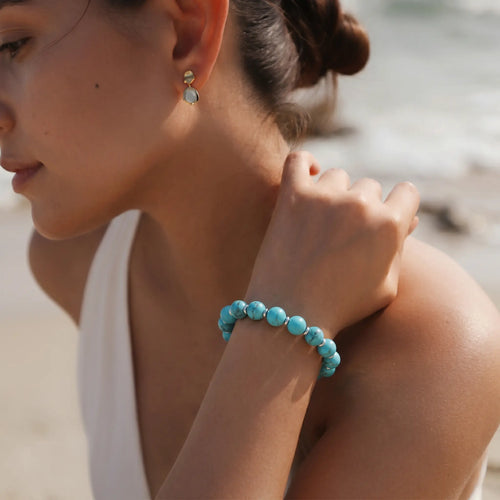 Downward high-angle shot from the left side showing a female hand touching her neck with a turquoise bracelet.