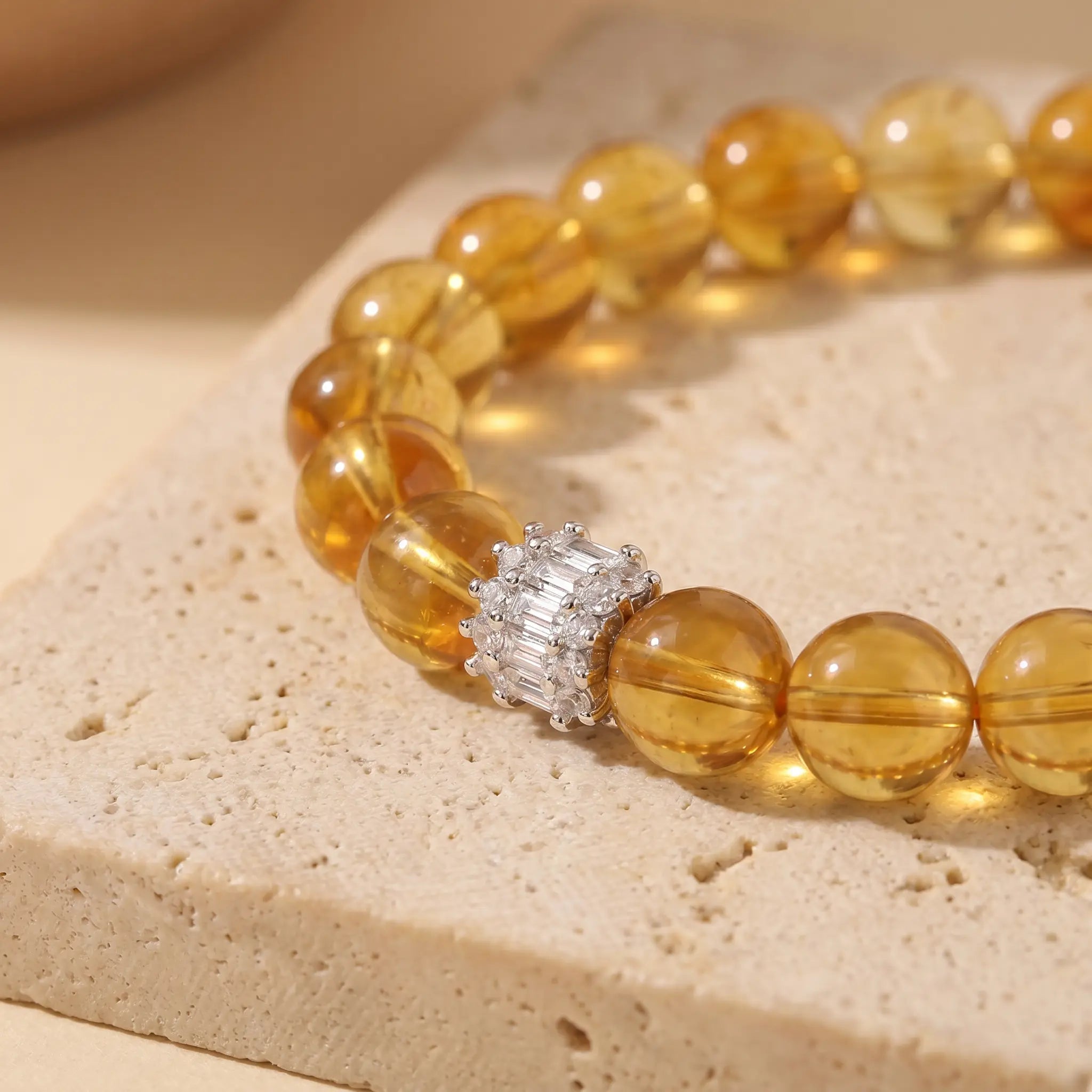 Macro shot of Solar Radiance Citrine Bracelet focusing on the natural textures of yellow crystal beads and the silver centerpiece over a travertine stone.