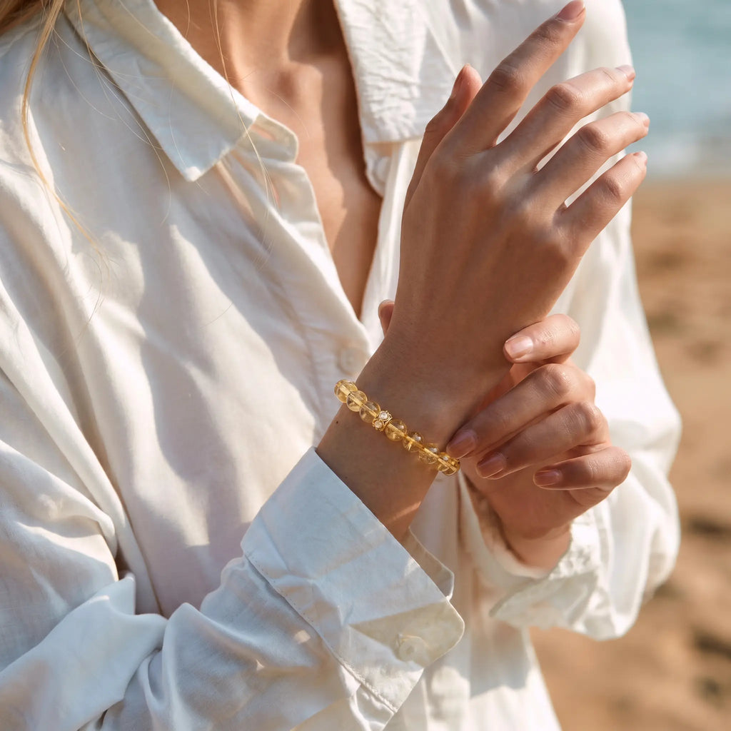 Low-angle side view of a right forearm raised to the chest while the left hand gently supports the crystal wrist bracelet.